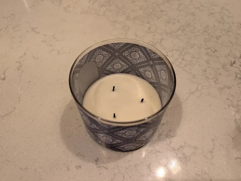 Source phone photo: a three-wick candle in a dark patterned glass jar on a kitchen counter